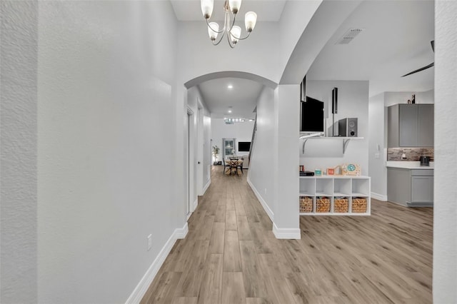 hall featuring arched walkways, a chandelier, light wood-style flooring, visible vents, and baseboards