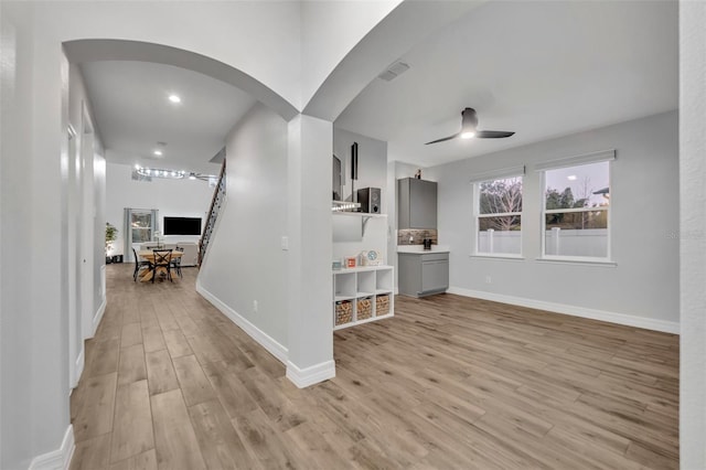 interior space with arched walkways, a ceiling fan, baseboards, visible vents, and light wood-style floors