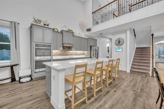 kitchen with gray cabinets, a center island with sink, and light wood-style flooring