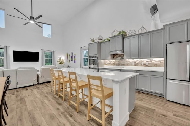 kitchen with light wood-style floors, a breakfast bar, gray cabinets, under cabinet range hood, and built in fridge