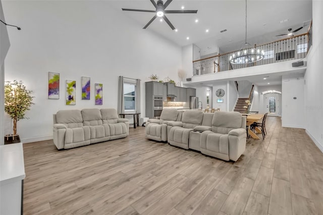 living area with light wood-type flooring, baseboards, stairway, and ceiling fan with notable chandelier