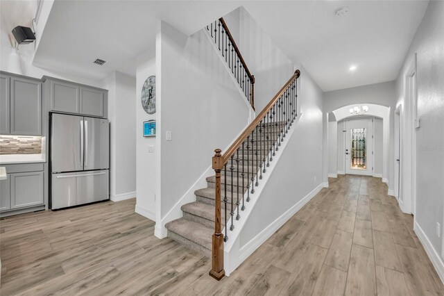 foyer entrance with arched walkways, light wood-type flooring, visible vents, and baseboards