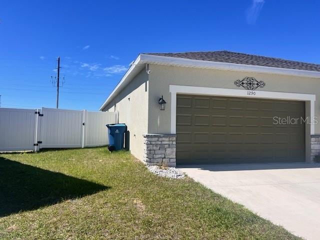 view of side of property with stone siding, concrete driveway, a lawn, a gate, and stucco siding