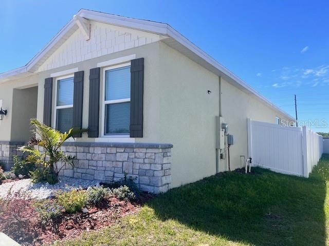 view of home's exterior featuring stone siding, fence, stucco siding, and a yard