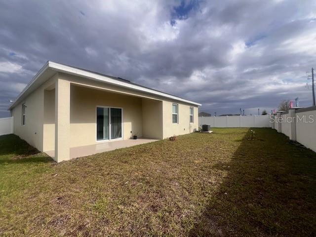 back of house featuring stucco siding, a fenced backyard, central AC unit, and a yard