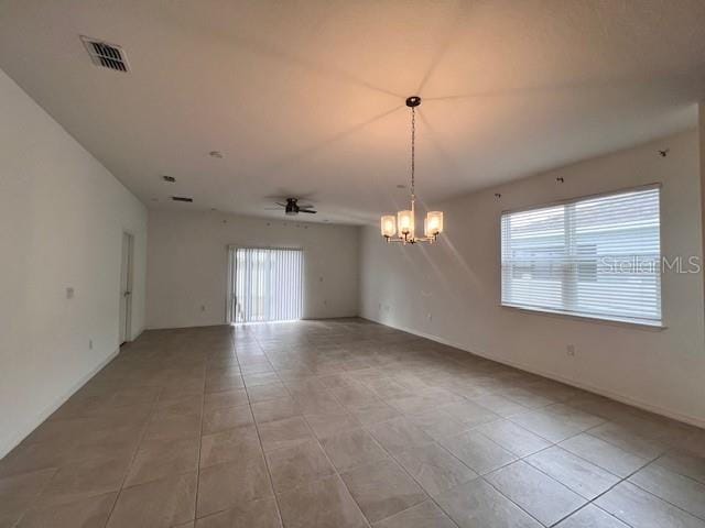 empty room with a healthy amount of sunlight, light tile patterned flooring, visible vents, and ceiling fan with notable chandelier