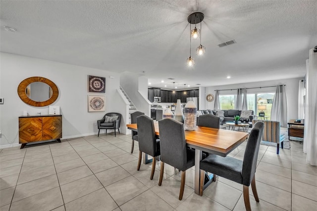 dining space with light tile patterned floors, visible vents, a textured ceiling, and stairs