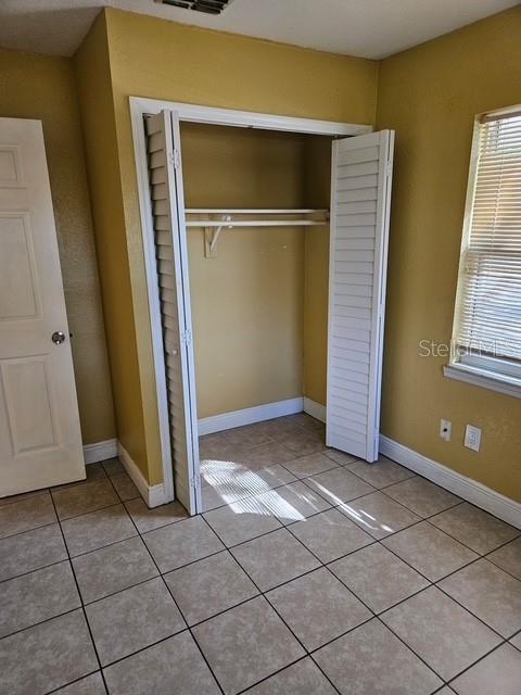 unfurnished bedroom featuring multiple windows, baseboards, a closet, and light tile patterned flooring