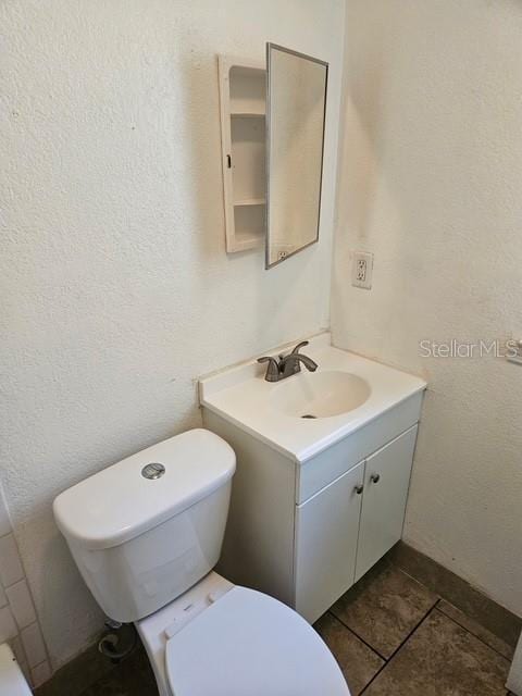 bathroom with a textured wall, vanity, toilet, and tile patterned floors