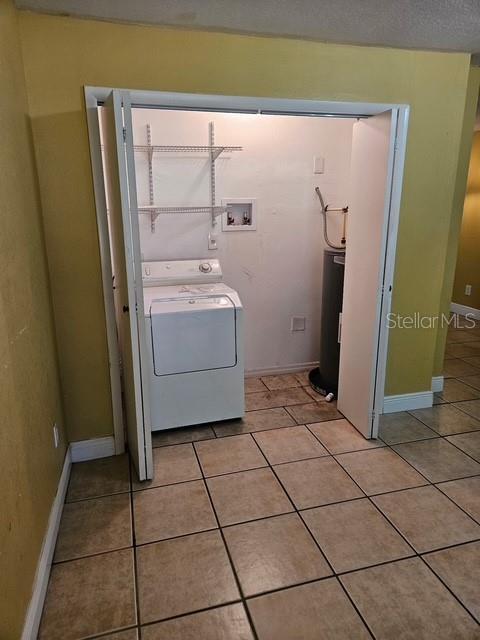 washroom featuring washer / dryer, light tile patterned floors, laundry area, baseboards, and water heater