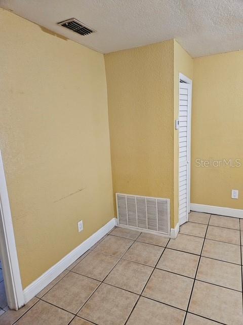 unfurnished room featuring baseboards, visible vents, a textured ceiling, and light tile patterned flooring