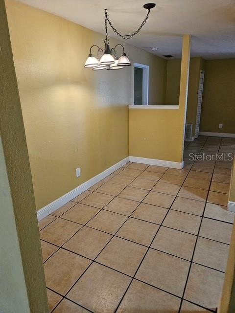 spare room with an inviting chandelier, baseboards, and light tile patterned flooring