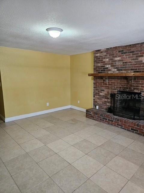 unfurnished living room with a textured ceiling, a brick fireplace, tile patterned floors, and baseboards