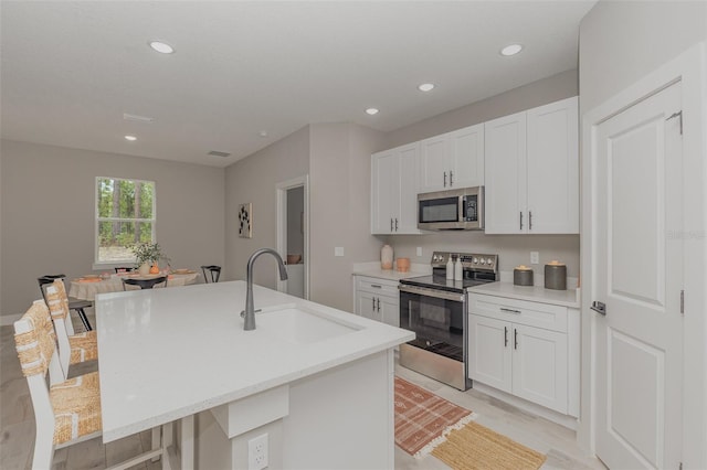 kitchen with stainless steel appliances, recessed lighting, white cabinetry, a sink, and an island with sink