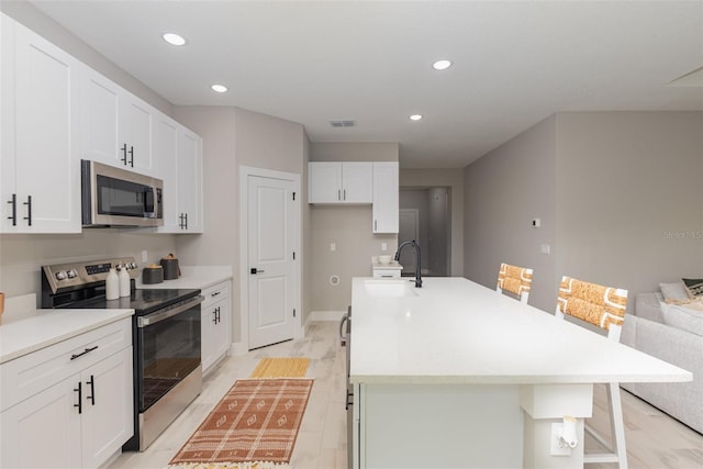 kitchen with appliances with stainless steel finishes, a kitchen island with sink, a sink, white cabinetry, and a kitchen bar