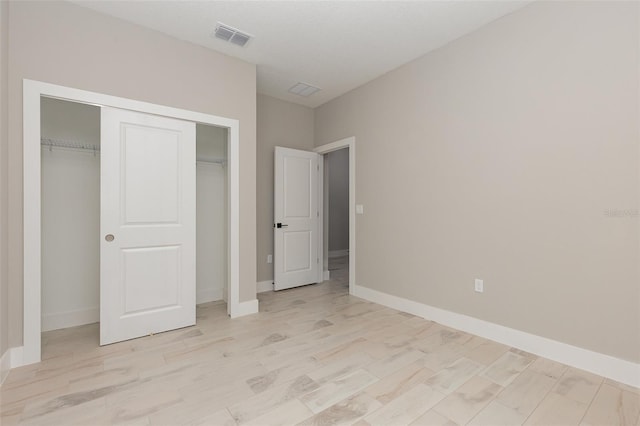 unfurnished bedroom featuring baseboards, visible vents, light wood-style flooring, and a closet