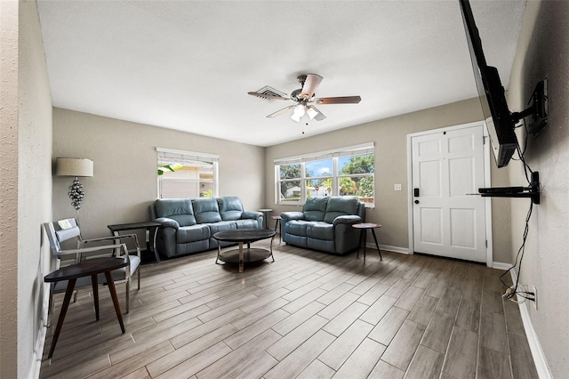 living room featuring a textured wall, wood finished floors, visible vents, a ceiling fan, and baseboards