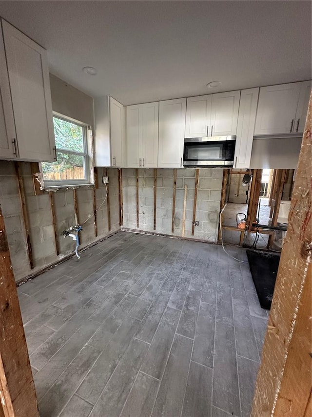 kitchen with stainless steel microwave, wood finished floors, and white cabinetry