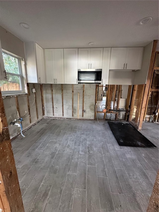 kitchen with stainless steel microwave, white cabinets, and wood finished floors