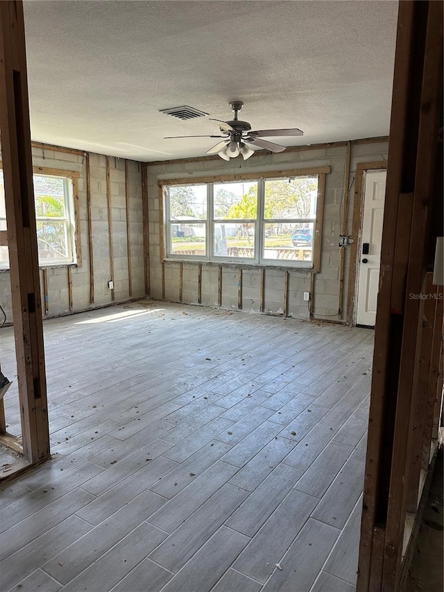 unfurnished room featuring concrete block wall, visible vents, a ceiling fan, hardwood / wood-style floors, and a textured ceiling