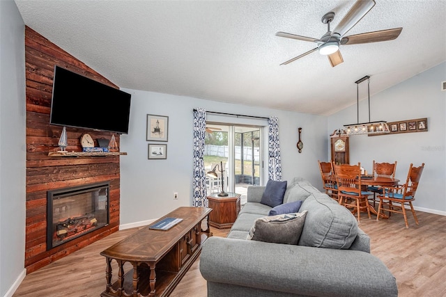 living area featuring lofted ceiling, light wood-style floors, a glass covered fireplace, ceiling fan, and a textured ceiling