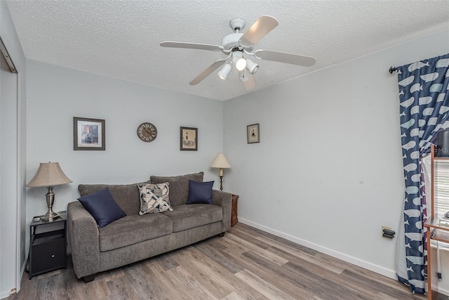 living area featuring a textured ceiling, ceiling fan, wood finished floors, and baseboards