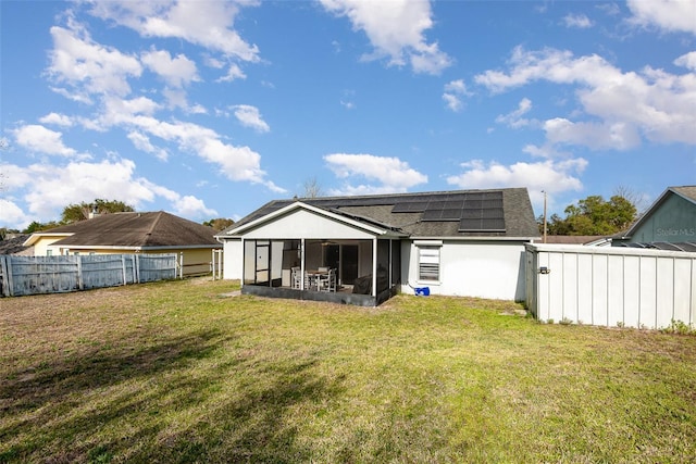 back of house featuring a sunroom, a fenced backyard, a lawn, and solar panels