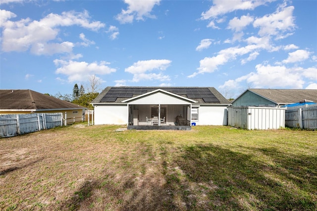 rear view of property with solar panels, a yard, a fenced backyard, and a sunroom