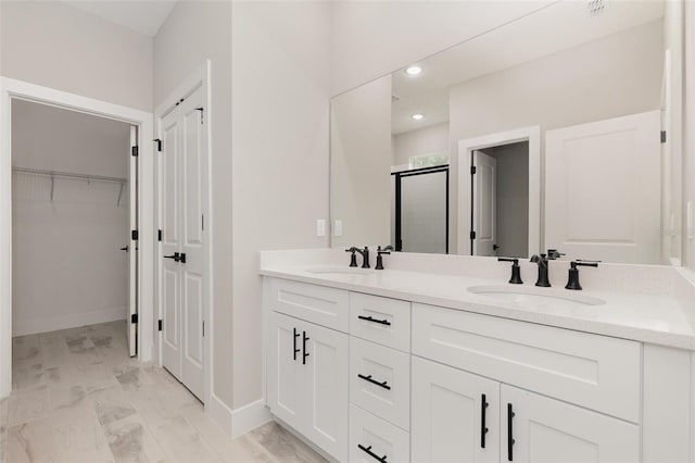 bathroom featuring a spacious closet, double vanity, a stall shower, and a sink