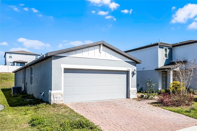 exterior space featuring a garage, stone siding, decorative driveway, stucco siding, and board and batten siding