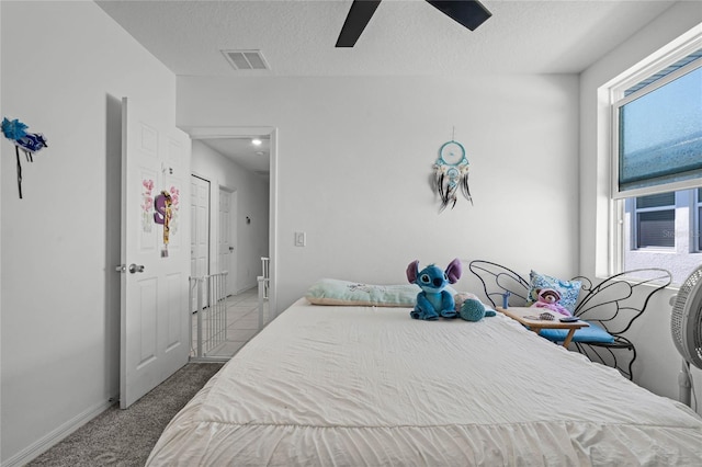 carpeted bedroom featuring a textured ceiling, baseboards, visible vents, and a ceiling fan