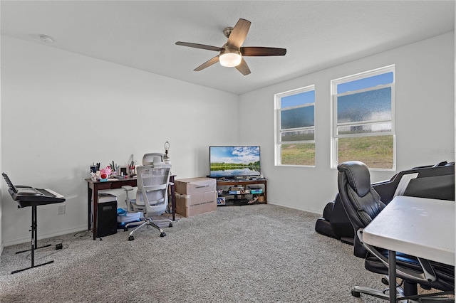 carpeted office space with a ceiling fan and baseboards