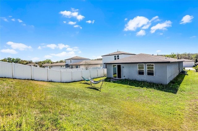 rear view of house featuring fence, a lawn, and stucco siding