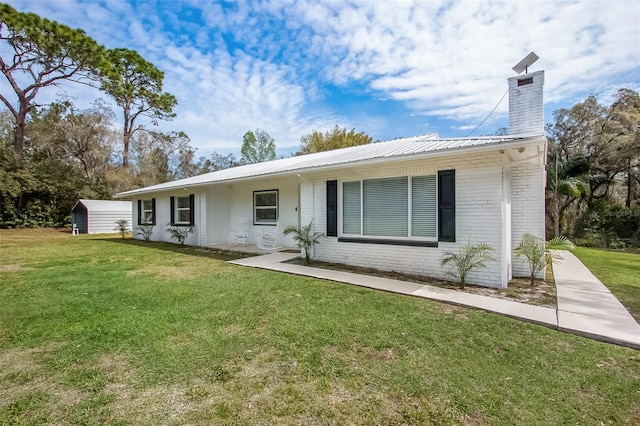 view of front of home with a front yard, brick siding, metal roof, and a chimney