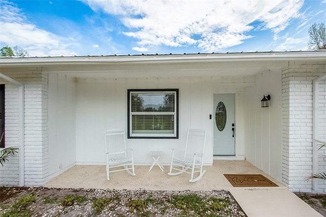 doorway to property with a porch and brick siding