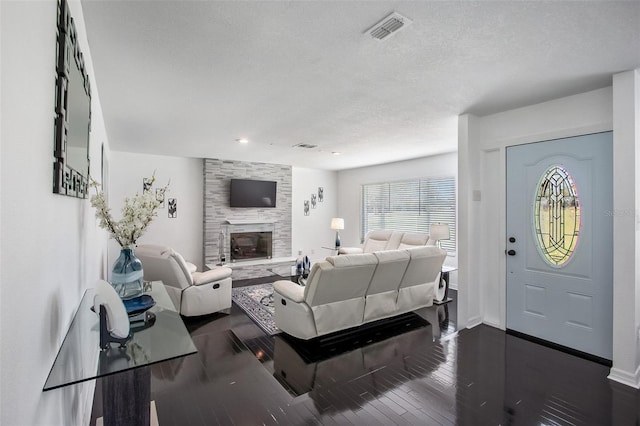 living room with a large fireplace, baseboards, visible vents, dark wood-type flooring, and a textured ceiling