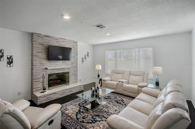 living room with a textured ceiling, a fireplace, wood finished floors, visible vents, and baseboards