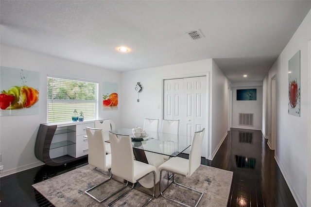 dining area with a textured ceiling, dark wood-style flooring, visible vents, and baseboards