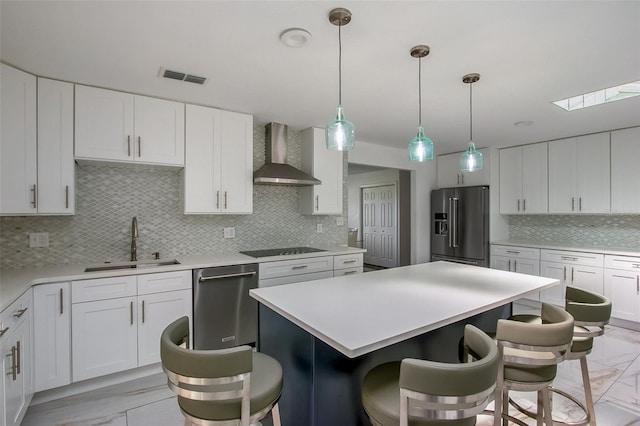 kitchen with wall chimney range hood, appliances with stainless steel finishes, marble finish floor, and a sink