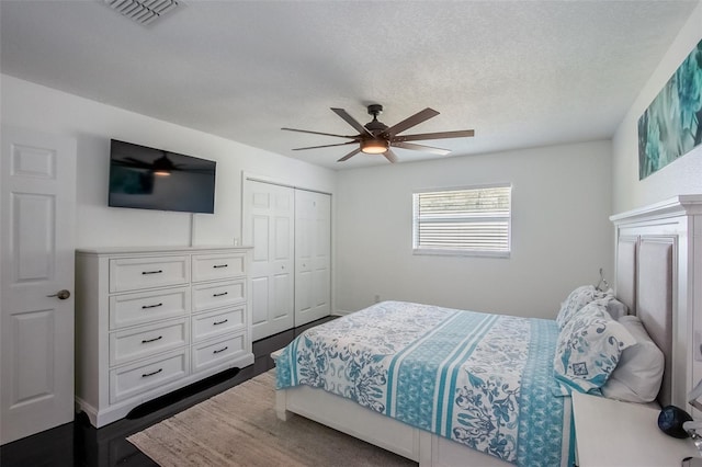 bedroom featuring ceiling fan, a textured ceiling, visible vents, a closet, and dark wood finished floors