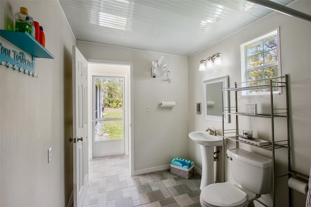 bathroom featuring stone finish flooring, a sink, toilet, and baseboards