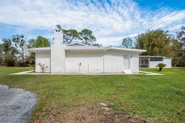 back of house with metal roof, a yard, a chimney, and stucco siding