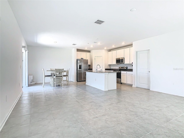 kitchen featuring visible vents, dark countertops, an island with sink, appliances with stainless steel finishes, and a sink