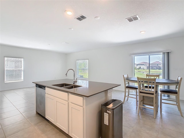 kitchen with a sink, visible vents, dishwasher, dark countertops, and a center island with sink