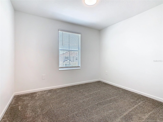 spare room with dark colored carpet and baseboards