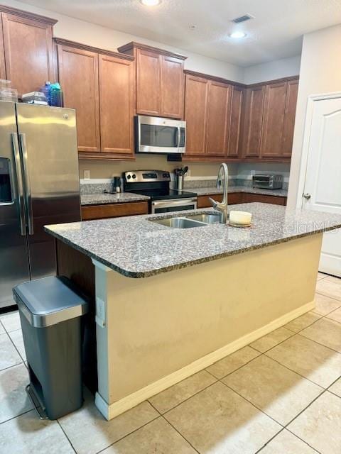 kitchen with an island with sink, stone countertops, stainless steel appliances, and light tile patterned flooring