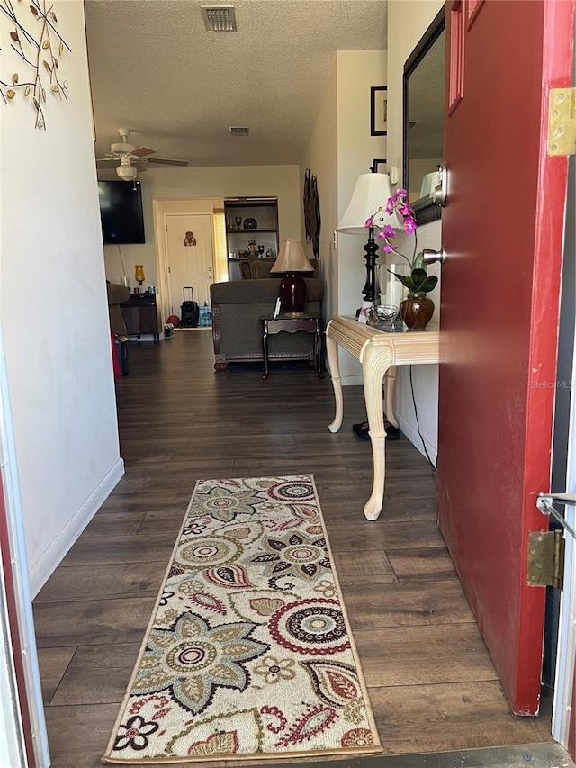 hallway with dark wood-style floors, visible vents, a textured ceiling, and baseboards