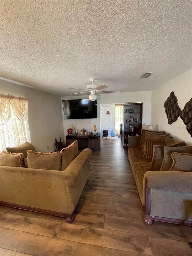 living room featuring visible vents, a textured ceiling, dark wood-style floors, and a ceiling fan