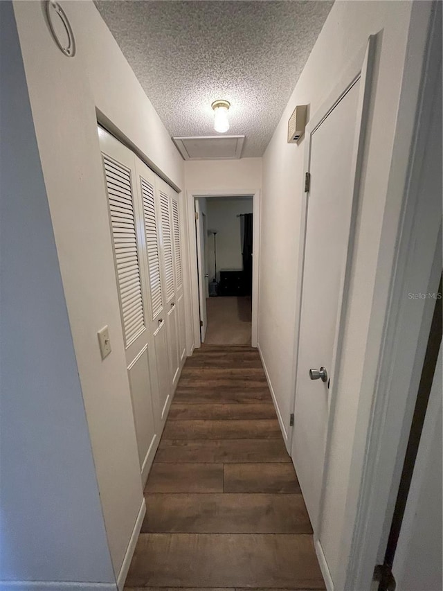 hall with attic access, a textured ceiling, baseboards, and dark wood-style flooring