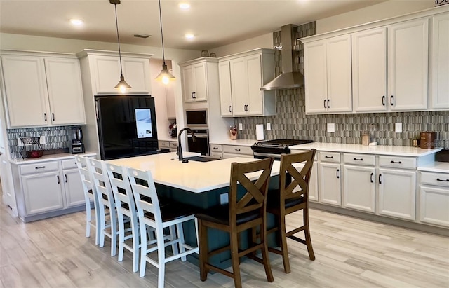 kitchen featuring refrigerator, a sink, a kitchen breakfast bar, wall chimney range hood, and light wood-type flooring